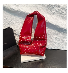 Red patent leather bag with silver rivets and knotted handle on white stone backdrop