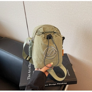 Detail of sage green nylon drawstring crossbody bag with embroidered D logo on a book
