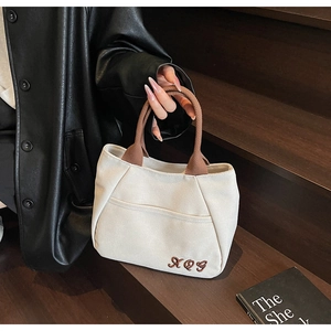 Close-up of beige canvas tote bag with brown XQY letter embroidery and sturdy webbing handles