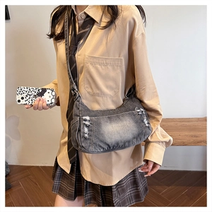 Detail of dark grey denim crossbody bag with distressed ripped edges and vintage wash style