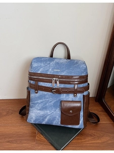 Blue denim backpack with brown leather trim displayed on a wooden table setup