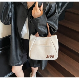 Detail view of canvas bucket bag featuring dark brown handles and embroidered XQG letters