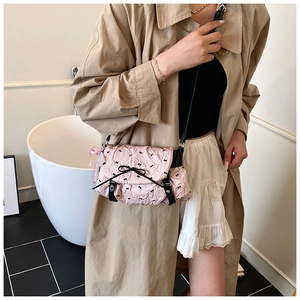 Detail of pink bow-patterned shoulder bag worn over a trench coat for a chic look