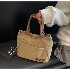 Detail of khaki canvas tote bag featuring brown woven handle and embroidered XOY logo