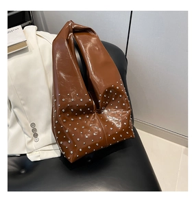 Close-up of brown patent leather tote bag with silver rivets on white blazer