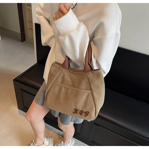 Close-up of brown canvas tote bag with letter embroidery and front pocket detail