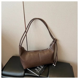 Detail of dark brown leather crescent bag featuring knot straps and metal ball accents