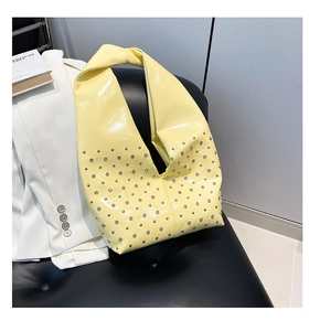 Detail of yellow rivet handbag with knotted handle on a black leather seat in office setting