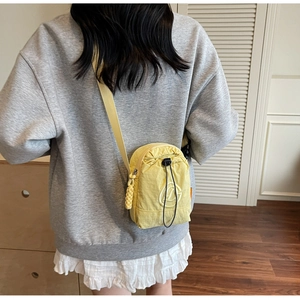Detail view of yellow nylon crossbody bag featuring round embroidered logo and adjustable strap