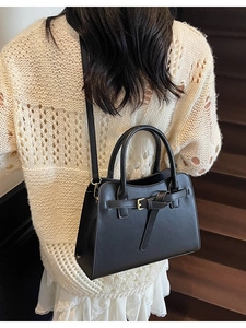 Minimalist black faux leather handbag with gold buckle shown on a model on stairs