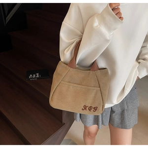 Detail showing the khaki canvas tote bag with brown handles and embroidered XQG initials