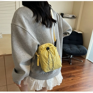 Close-up of yellow nylon crossbody bag with drawstring pocket and embroidered logo