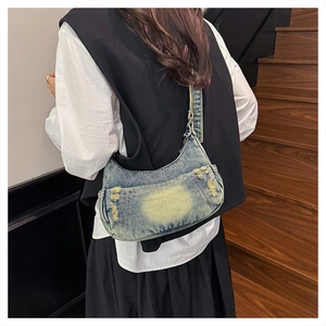 Detail of blue and yellow washed denim crescent bag with distressed fringe texture on strap