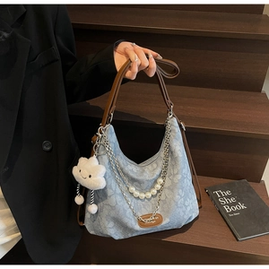Close-up of denim floral bag with pearls, metal chains and brown leather strap details
