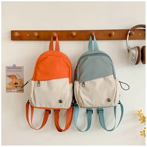 Détail de mini sacs à dos en toile bleu et orange suspendus sur cintres en bois
