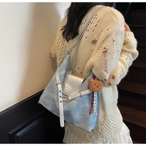 Blaue Denim-Tragetasche mit Kettenriemen und Bärenanhänger an der Schulter des Models