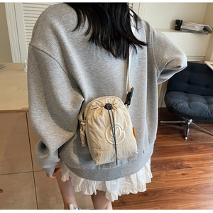 Close-up of beige nylon crossbody bag featuring drawstring closure and round logo embroidery