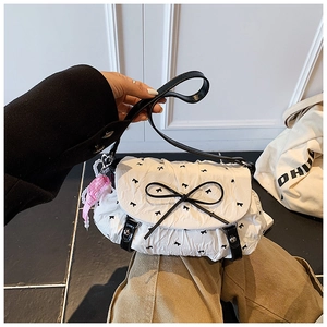 Detail of white pleated bag featuring black bows, leather strap and pearl charm accessory