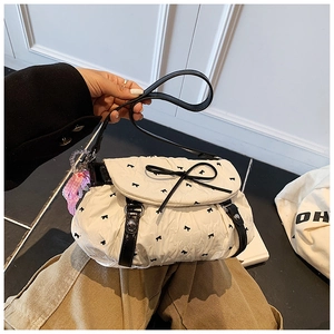 Detail of white pleated handbag featuring mini black bows and a pink plaid charm