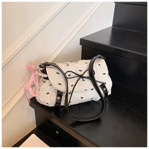 Detail of white ruffled crossbody bag featuring black bows and pearl charm accessory