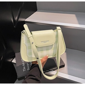 Détail d'un sac bandoulière en cuir vert clair et tissu écossais avec lettrage élégant