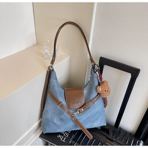 Detail der Jeans-Tote mit brauner Lederklappe und Bärenanhänger auf schwarzem Koffer