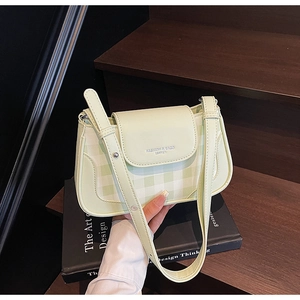 Détail d'un sac bandoulière vert clair à carreaux posé sur des livres vintage