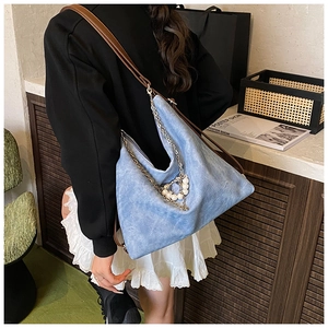 Detail of blue denim tote bag with decorative pearl chain and adjustable leather strap
