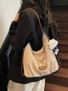 Beige canvas hobo shoulder bag with pearl chain strap and plush charm worn by model