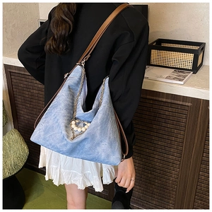 Detail of blue denim hobo bag with pearl heart pendant and golden chain strap