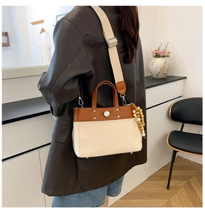 Detalle del bolso tote de lona y cuero con remaches metálicos y dije de cuentas de madera