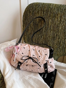 Pink pleated crossbody bag with black bows and pearl ribbon charm on a green chair