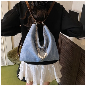 Back view of light blue denim tote with pearl chain and bow charm on a model's shoulder