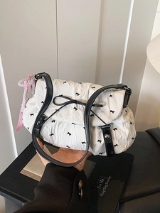 White pleated crossbody bag with black bow prints and a pink ribbon pearl charm