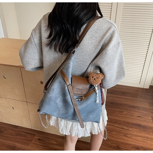 Details der graublauen Shopper-Tasche mit Lederriemen und braunem Bären-Anhänger