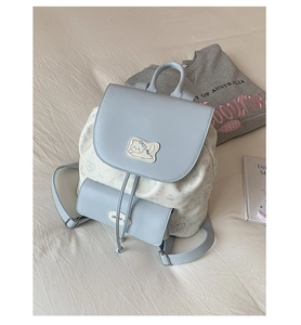 Détail d'un sac à dos bleu clair avec broderie de chat et motifs floraux sur un lit