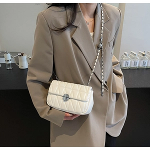 White quilted crossbody bag with silver chain strap and adjustable ball on a brown blazer