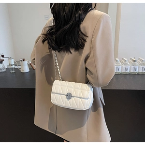Detail of a white quilted crossbody bag with silver chain strap and metal lock closure