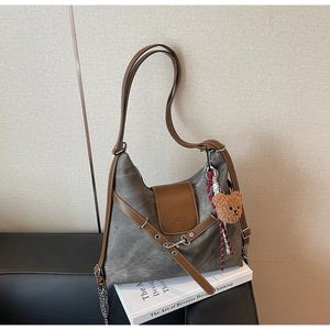 Detail der grauen Vintage-Canvas-Tasche mit braunem Lederbesatz und süßem Bären-Anhänger