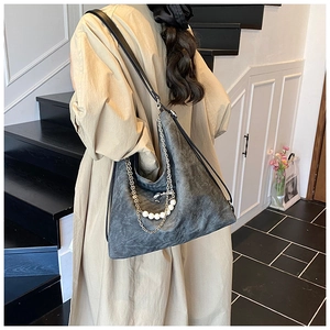 Detail of dark grey hobo bag featuring pearl and metal chain straps on model