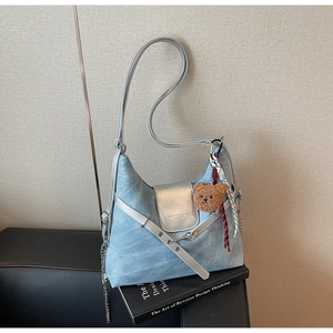 Detail der hellblauen Denim-Tasche mit Lederriemen, Bärenanhänger und Kettenverzierung