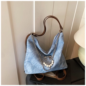 Detail of blue denim hobo bag with pearl chain, silver bow charm, and brown leather strap
