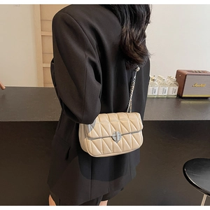 Close-up of quilted cream crossbody bag with silver chain strap worn by a model