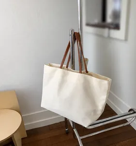 Detail of minimalist canvas tote bag featuring cream fabric and brown leather handles