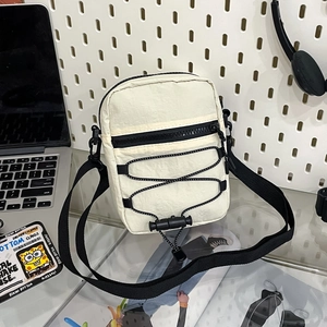 Detail of off-white nylon crossbody bag with black drawstring and front zipper pocket