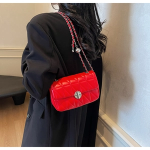 Detailed close-up of red quilted leather crossbody bag featuring silver metal chain and orb charm