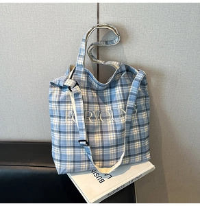 Detail of blue plaid canvas tote bag showing embroidery and adjustable shoulder strap