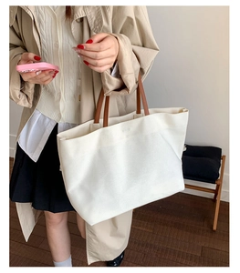 Minimalist white canvas tote bag with brown leather straps shown on a model's shoulder