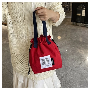 Detail view of a red canvas drawstring lunch bag with blue handle and artistic soul label