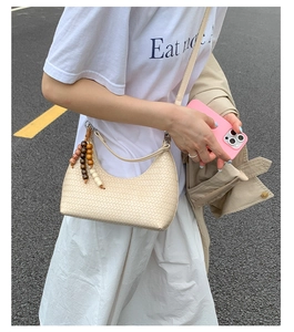 Detail of cream woven crescent underarm bag with wooden bead charm and crossbody strap